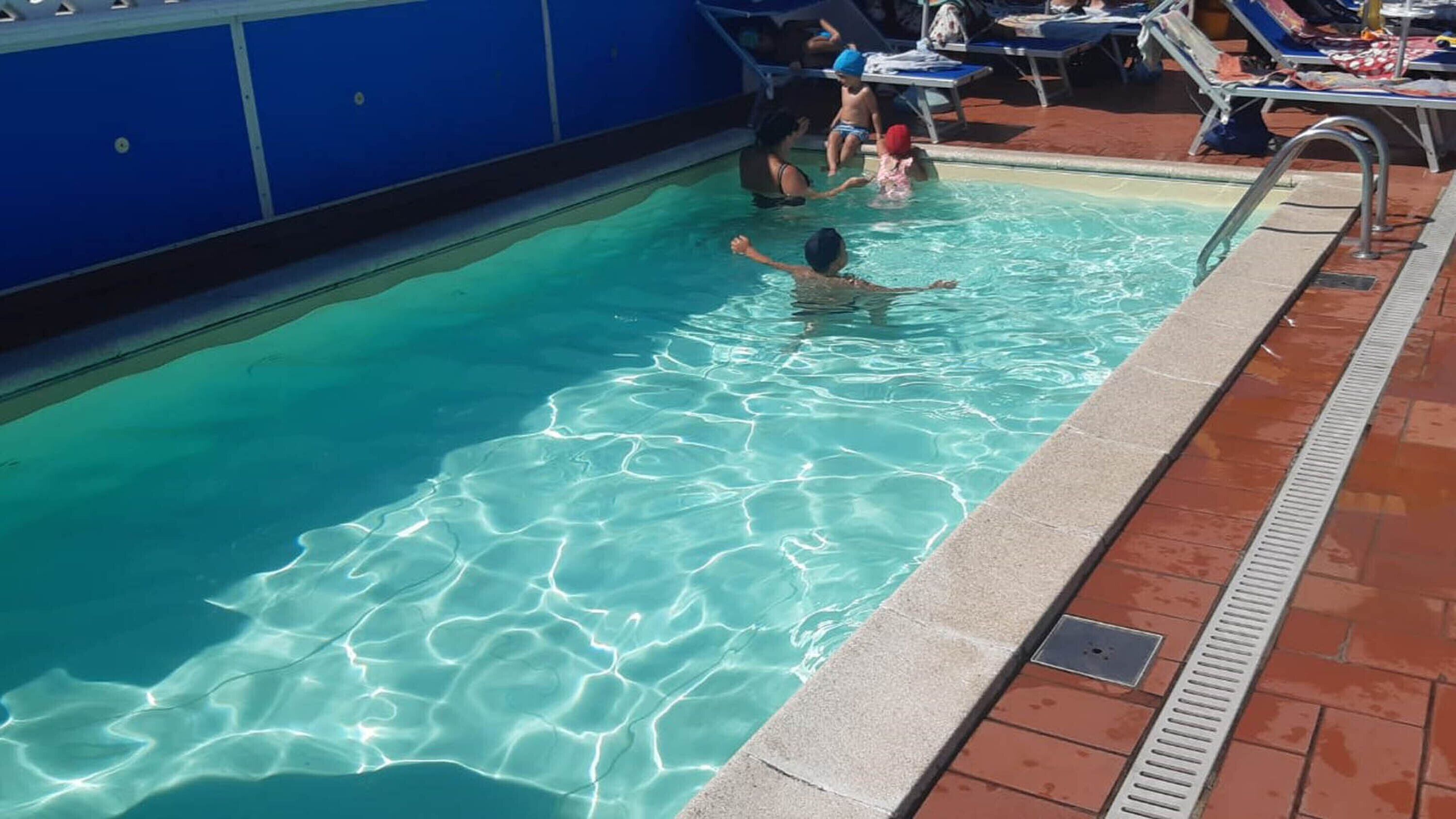 Piscina com água cristalina, rodeada por espreguiçadeiras e um deck revestido de azulejos.