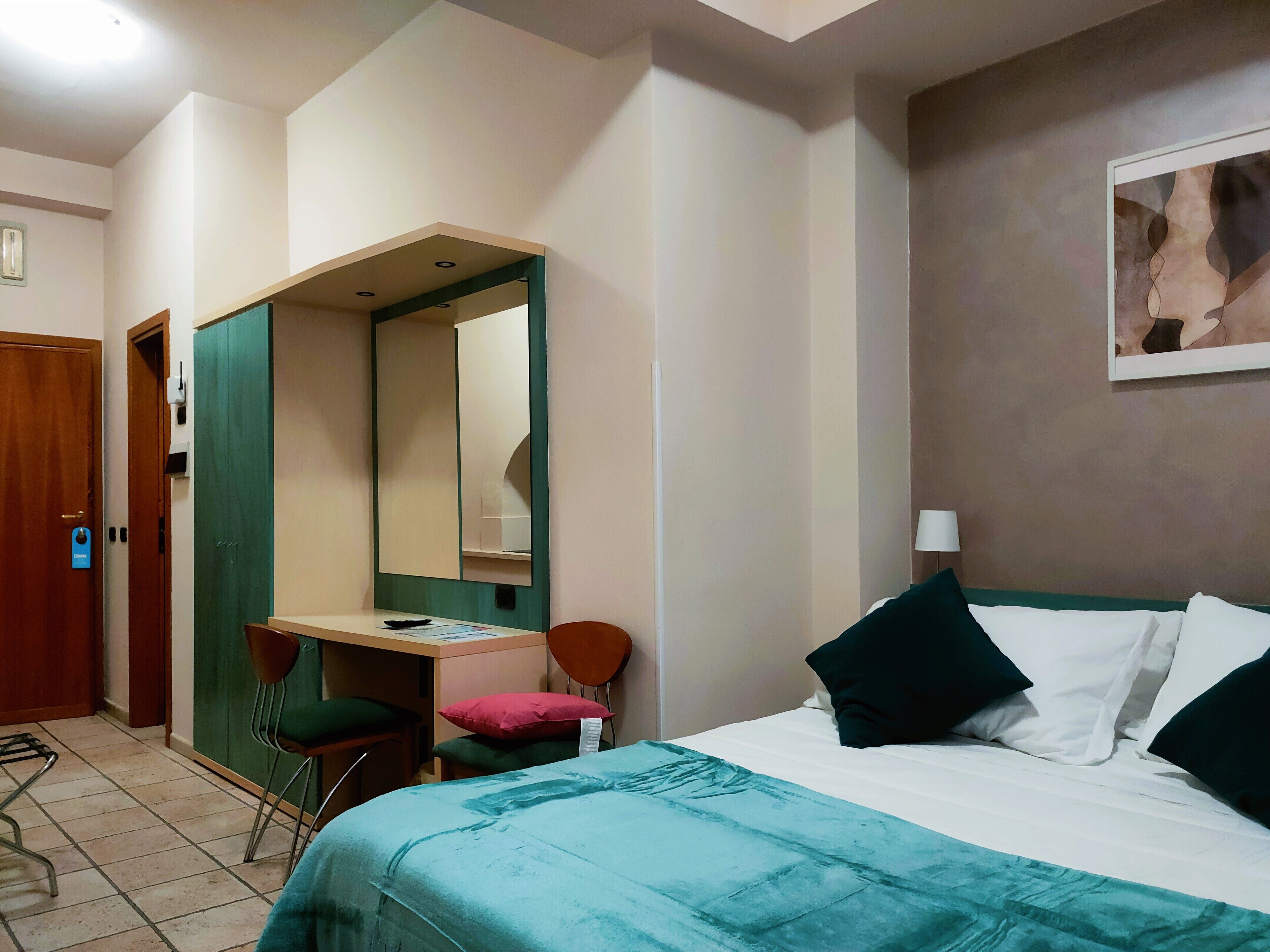 Une chambre d’hôtel équipée d’un lit, d’un bureau, d’une chaise, d’un miroir et d’une œuvre d’art accrochée au mur.