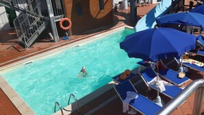 Una piscina con un flotador salvavidas, sillas de descanso y sombrillas.