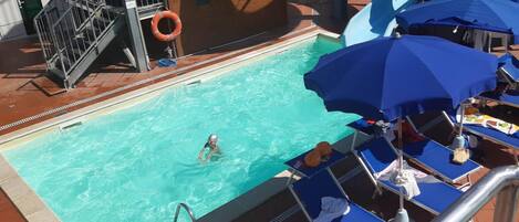 Ein Schwimmbecken mit Rettungsboje, Liegestühlen und Sonnenschirmen.