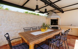 An outdoor dining area with a wooden table and chairs, a stone wall, and a built-in grill. - Awesome home in Pula with sauna (Pula)