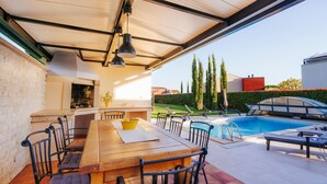 An outdoor patio with a wooden table and chairs, a barbecue grill, and a swimming pool. - Awesome home in Pula with sauna (Pula)