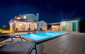 Une maison moderne dotée d’une piscine, d’un espace salon extérieur et d’un patio couvert.