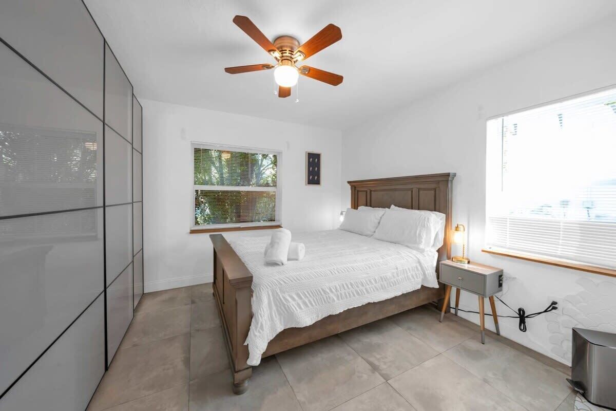 A bedroom with a bed, a ceiling fan, a bedside table, and a window.