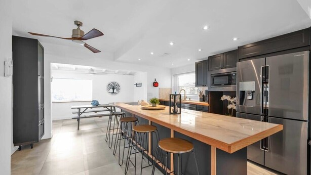 A modern kitchen with a central island, bar stools, stainless steel appliances, and a ceiling fan. - Biscayne Shore-Stylish 3BR Tropical Family Retreat (Miami)