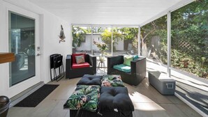 A covered patio area with wicker furniture, a red cushioned chair, and a small table with a vase. - Biscayne Shore-Stylish 3BR Tropical Family Retreat (Miami)