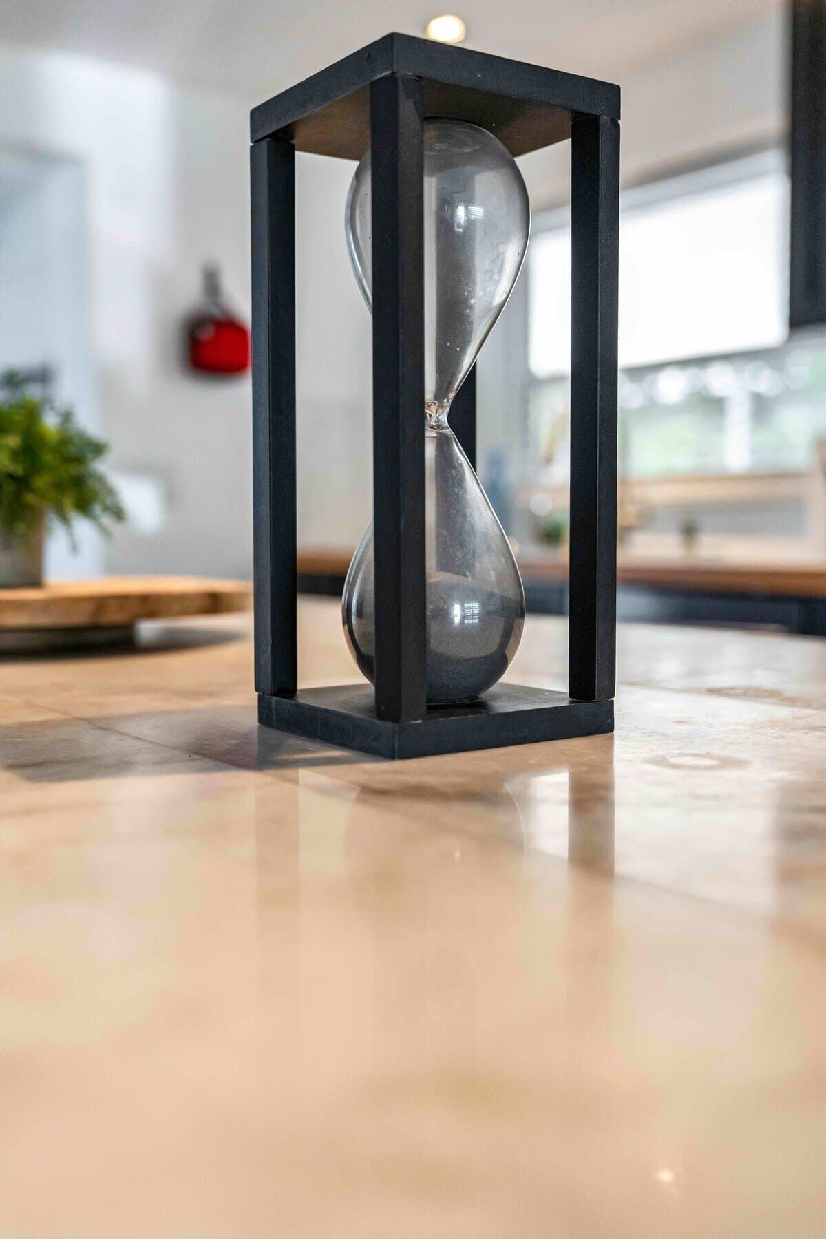 A modern hourglass with a black frame on a polished floor.