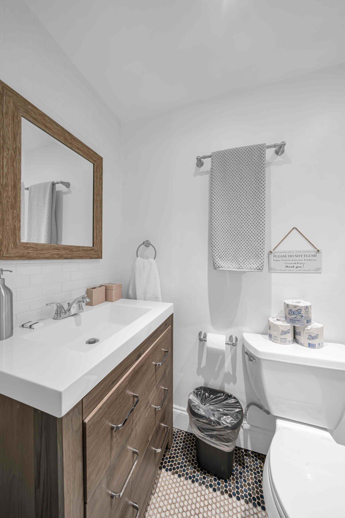 A modern bathroom with a white sink, wooden vanity, and a toilet. There are towels and toilet paper on the wall.
