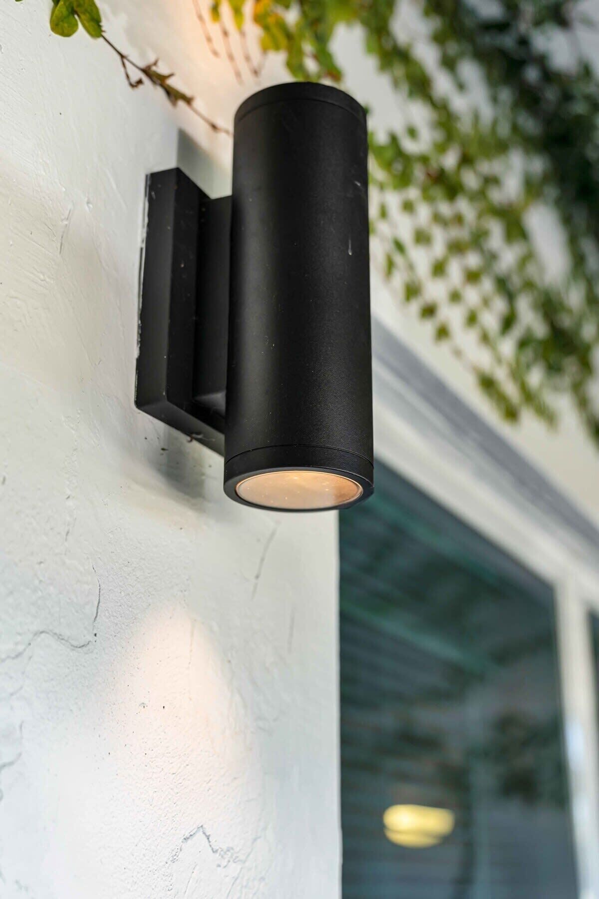 Un luminaire extérieur noir, fixé au mur, est installé sur un mur blanc.