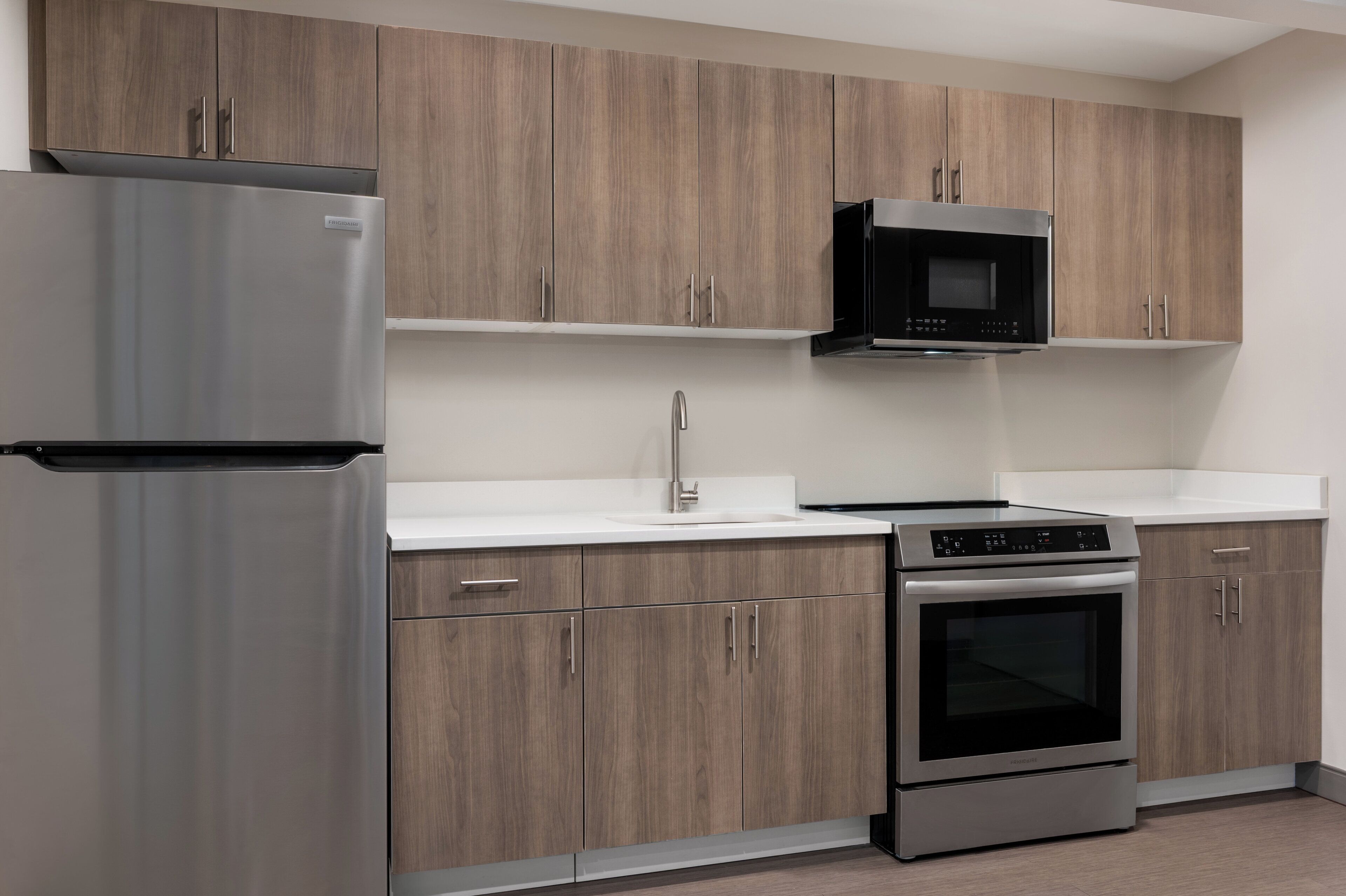 A modern kitchen with stainless steel appliances, wooden cabinets, and a white countertop.
