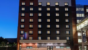 A multi-story hotel with a modern design, featuring a mix of brick and dark panel exteriors, and a visible entrance with a glass door. - Holiday Inn Express & Suites Bronx - Barnabas area by IHG (Bronx)