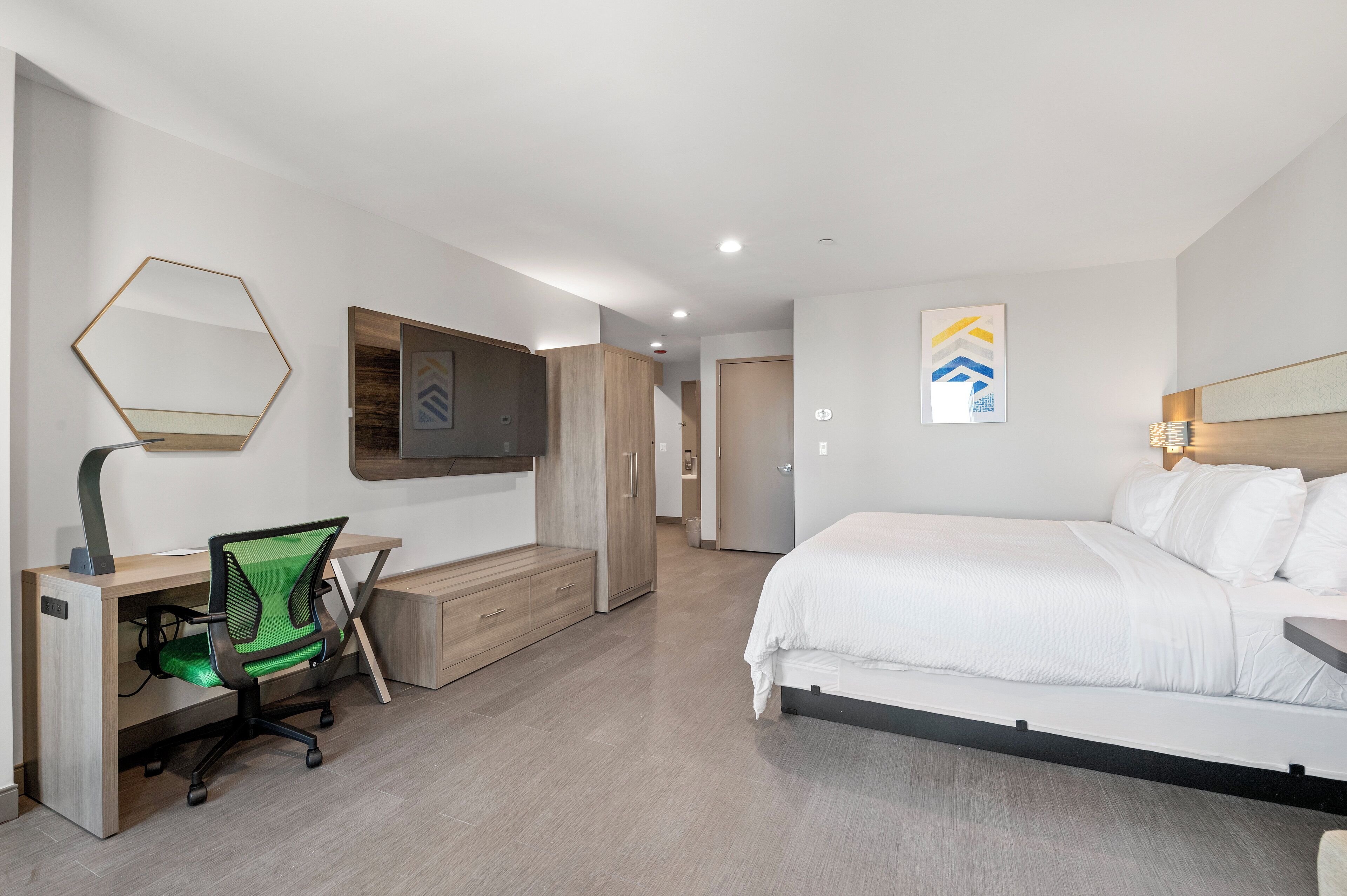 A modern hotel room with a bed, a desk with a chair, a wardrobe, and a television.