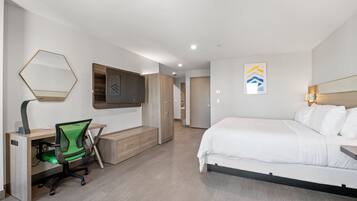 A modern hotel room with a bed, a desk with a chair, a wardrobe, and a television.
