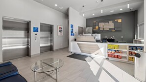 A modern reception area with a white counter, a glass table, and two elevators. - Holiday Inn Express & Suites Bronx - Barnabas area by IHG (Bronx)