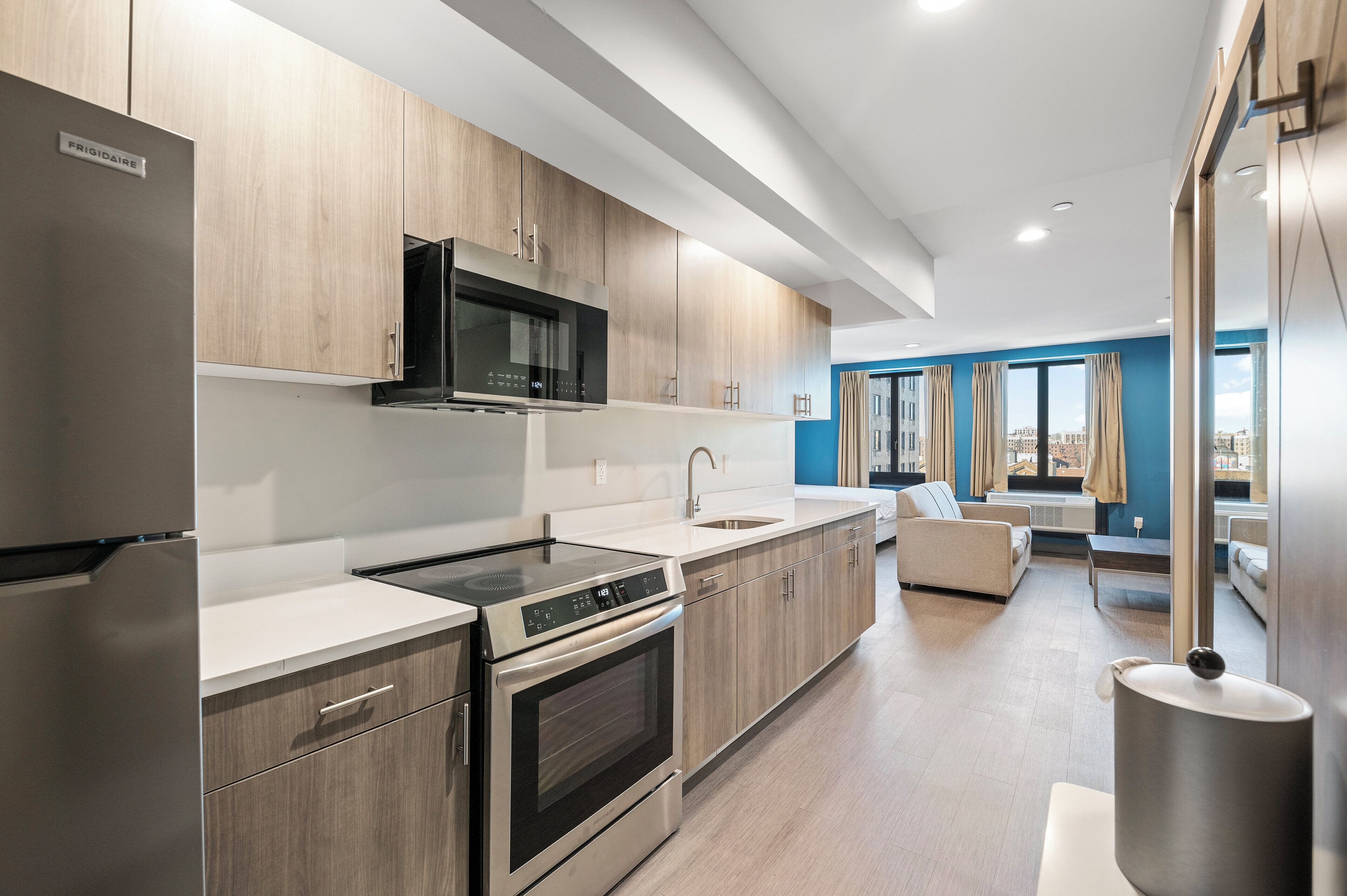 Une cuisine moderne dotée d’appareils électroménagers en acier inoxydable, de meubles en bois et d’une grande fenêtre offrant une vue sur la ville.