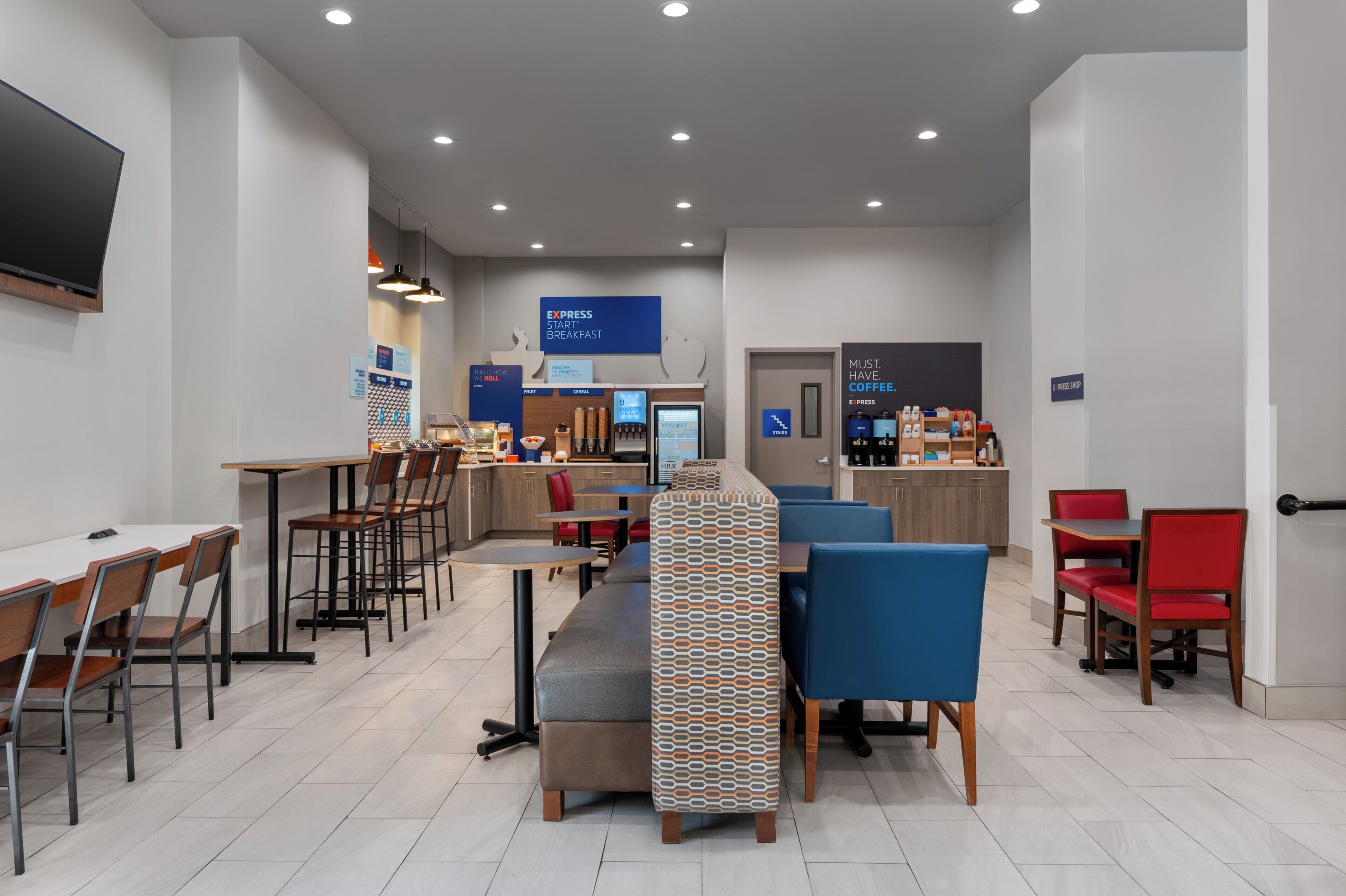 Un café moderne avec des tables et des chaises, un comptoir où l’on sert du café, et un panneau indiquant l’espace réservé aux petits-déjeuners.
