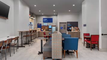 Un café moderne avec des tables et des chaises, un comptoir où l’on sert du café, et un panneau indiquant l’espace réservé aux petits-déjeuners.