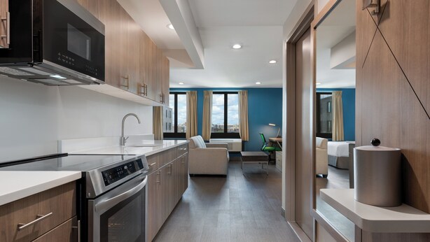 A modern kitchen with stainless steel appliances, wooden cabinets, and a view of the city through large windows. - Holiday Inn Express & Suites Bronx - Barnabas area by IHG (Bronx)