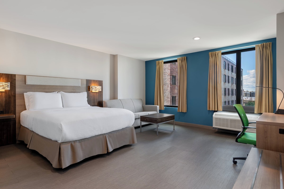 Ein Hotelzimmer mit einem großen Bett, einem Schlafsofa, einem Schreibtisch und einem Sessel.