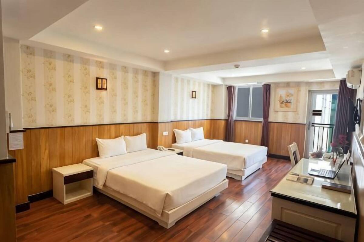 A hotel room with two beds, a desk, a chair, a small table, and a window.