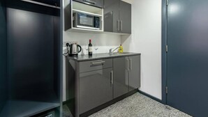 A compact kitchen with a microwave, kettle, wine glass, and dish soap on the counter. - Stylish 1-bed Studio - Heart of Nottingham (Nottingham)