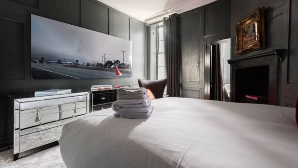 A modern hotel room with a large bed, a flat-screen TV, a dresser, and a fireplace.