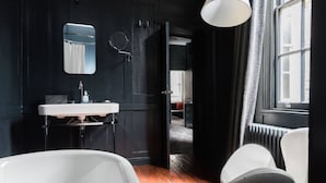 A modern bathroom with a white bathtub, a sink, and a mirror. There is a door leading to another room.
