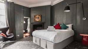 A modern bedroom with a large bed, a fireplace, a chair, and a desk.