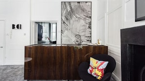 A modern reception desk with a dark wood finish, a black chair with a colorful cushion, and a large abstract artwork on the wall.