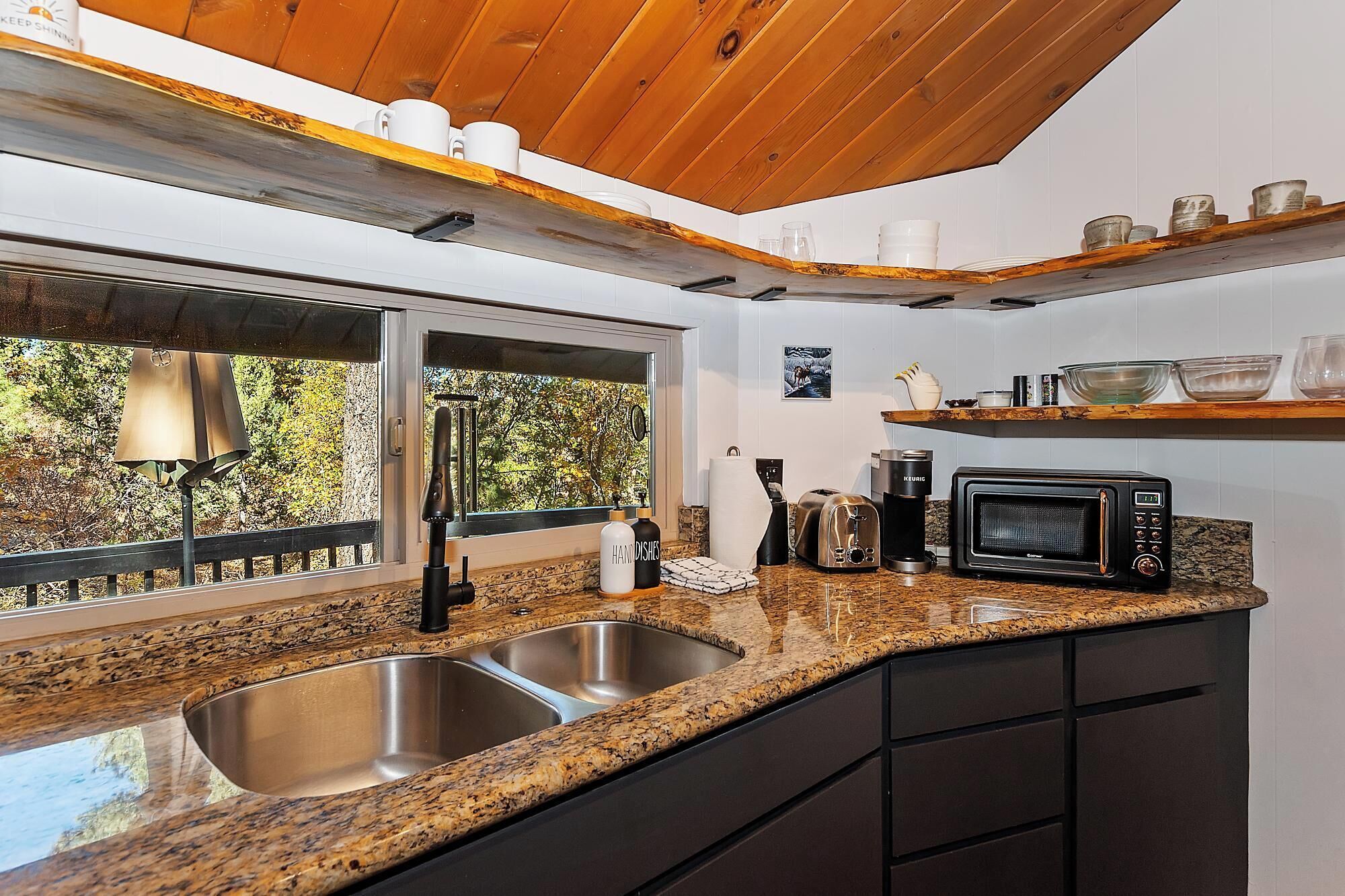 A kitchen with granite countertops, stainless steel sinks, a coffee maker, and a microwave.