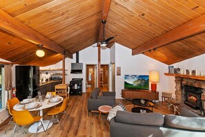 A spacious loft with a high ceiling, a dining area with yellow chairs, a gray sofa, a fireplace, and a kitchen in the background.