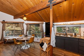 A modern kitchen with a large window, wooden ceiling, and a dining area with a table and chairs.
