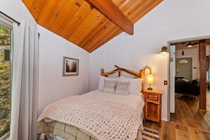 A bedroom with a wooden ceiling, a bed with a white blanket, a bedside lamp, and a picture on the wall.