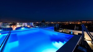 A rooftop pool with glass railings and a city view at night.