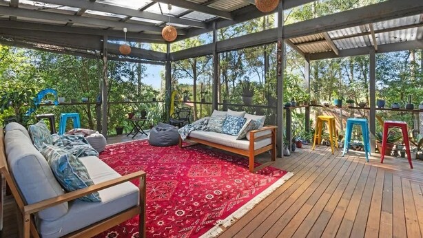 A covered outdoor seating area with a sofa, a red patterned rug, and colorful stools.