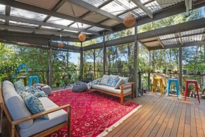 A covered outdoor seating area with a sofa, a red patterned rug, and colorful stools. - The Arthouse at Mossy (Mossy Point)
