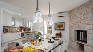 Una cocina moderna con armarios blancos, una pared de acento de ladrillo, una zona de comedor con una mesa y sillas blancas, y una chimenea.