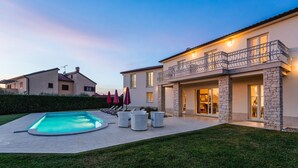 Una casa moderna con piscina, mobiliario exterior y fachada de piedra.