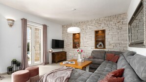 Una sala de estar moderna con una pared de piedra, un sofá gris, una mesa de centro de madera y un televisor instalado en la pared.