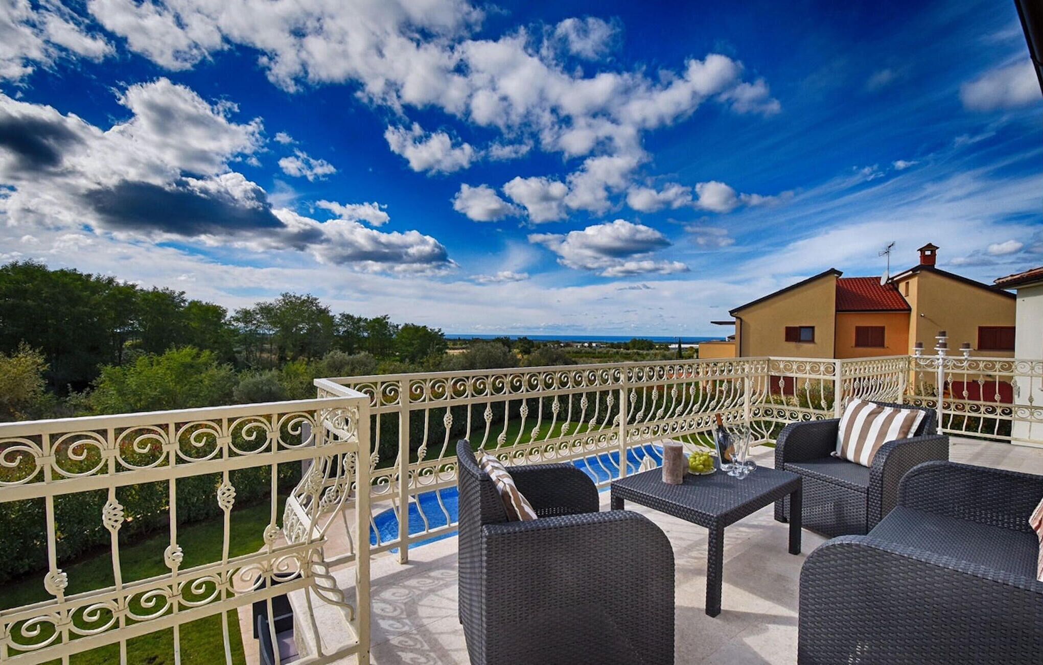 Ein Balkon mit Korbmöbeln, einem Pool und Blick auf ein Haus und die Landschaft.