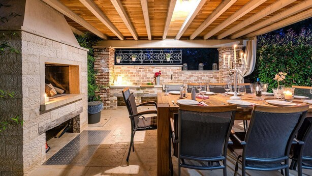 Un área de comedor al aire libre con chimenea de piedra, vigas de techo de madera y pared de ladrillo.
