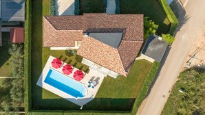 Vista aérea de una propiedad con piscina, sombrillas rojas y tejado de baldosas.