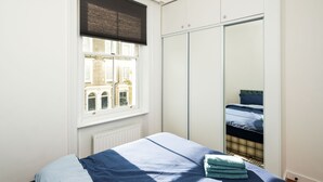 A bedroom with a bed, a window with blinds, a radiator, and a wardrobe. - Charming 2-bed Apartment in London (London)