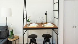 A dining area with a wooden table set for two, black stools, a lamp, and a potted plant. - Charming 2-bed Apartment in London (London)