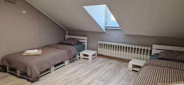 Un dormitorio pequeño y moderno con techo inclinado y tragaluces, con dos camas con ropa de cama a rayas y un radiador blanco.