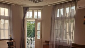 A room with a wooden floor, a bed with a pink bedspread, a desk with a chair, and a window with curtains. - Lambo's Corner  (Varna)