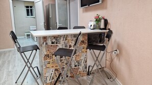 A small, modern room with a white table, four foldable chairs, a flat-screen TV, and a coffee maker. - Lambo's Corner  (Varna)