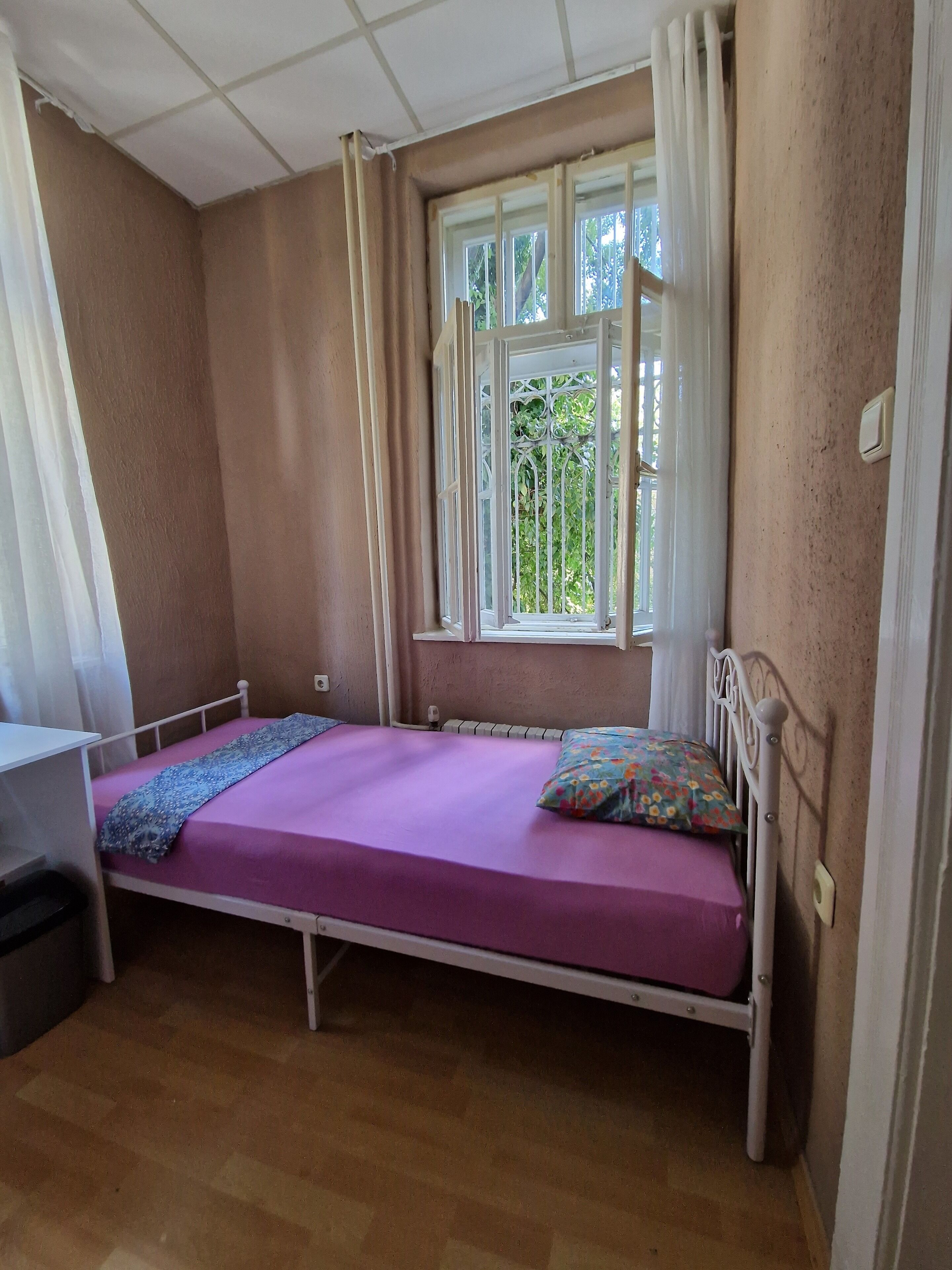 A single-bed room with a window, a desk, and a chair.