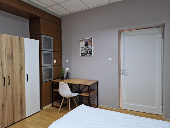 Un dormitorio con cama, escritorio, silla, armario y puerta.