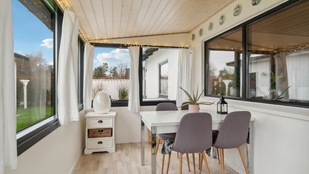 Een kleine kamer met een eettafel, twee stoelen, een klein wit kastje en een potplant.